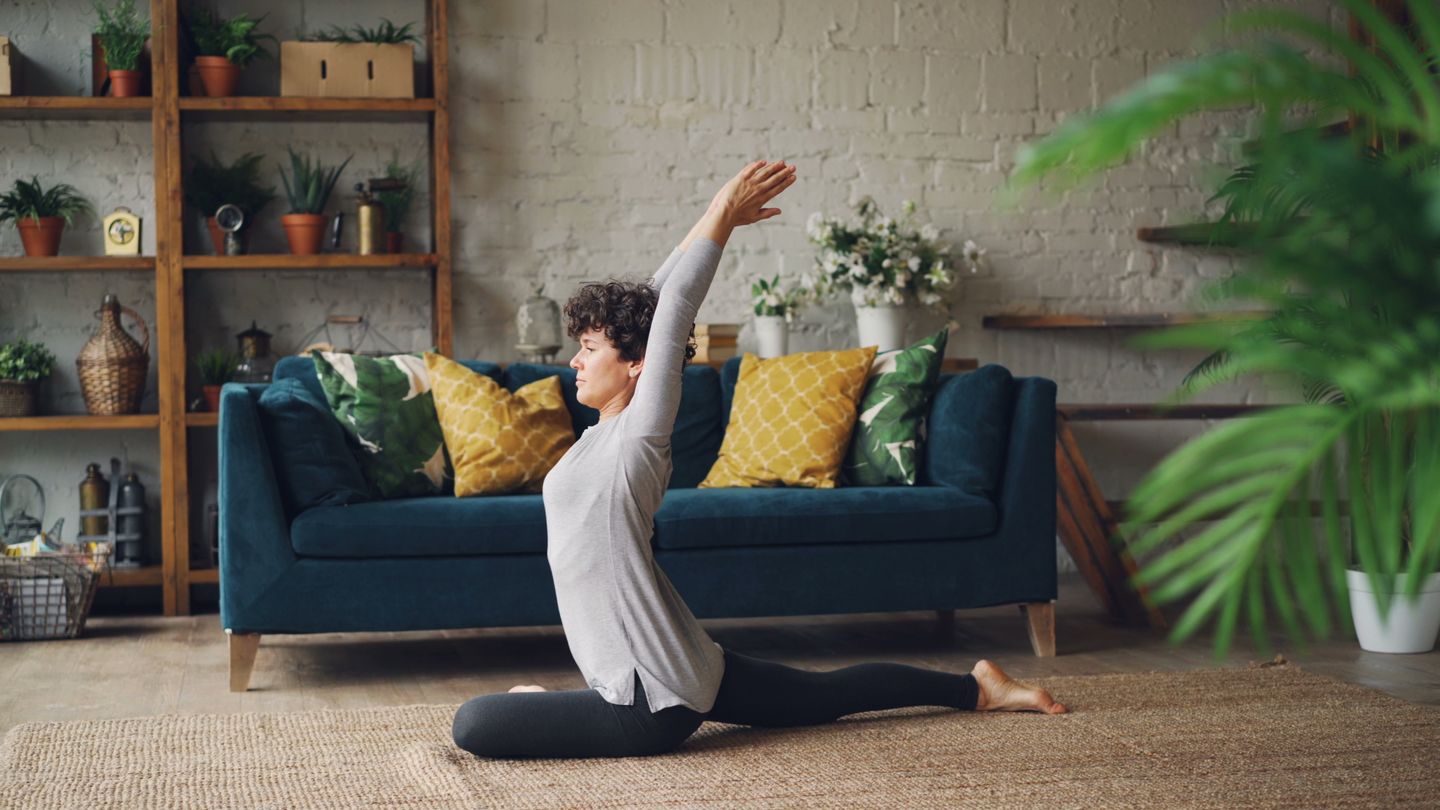 A woman practicing yoga indoors with plants and cozy decor creating a serene atmosphere.