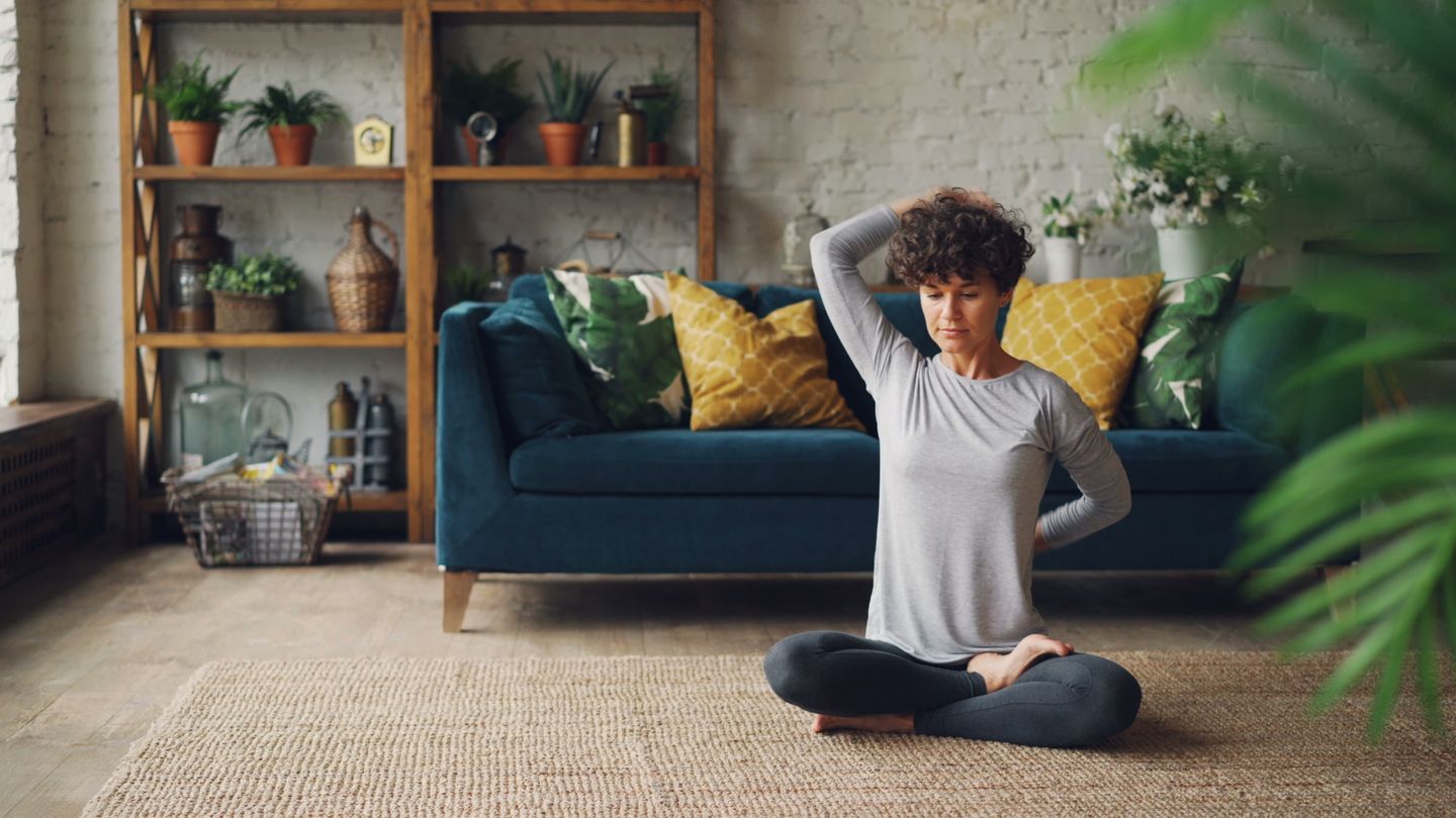 A woman meditating in a stylish, plant-filled living room for relaxation and wellbeing.