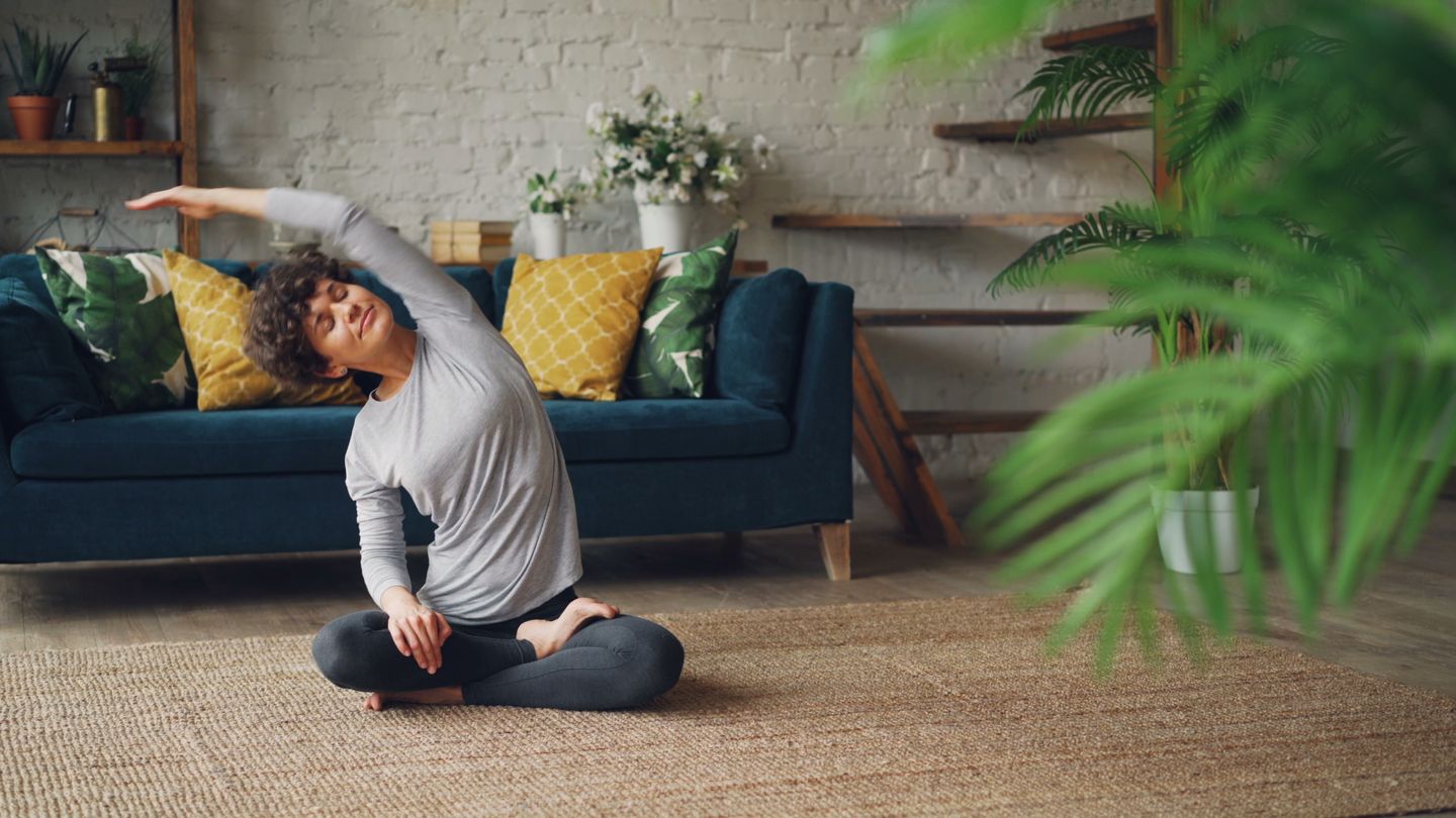 Woman doing a yoga pose on a rug in a cozy living room with plants.